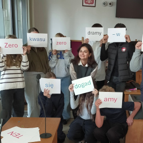 Mediator Daria Bezwińska wraz uczniami podczas warsztatów. Uczniowie trzymają kartki, które tworzą hasło  